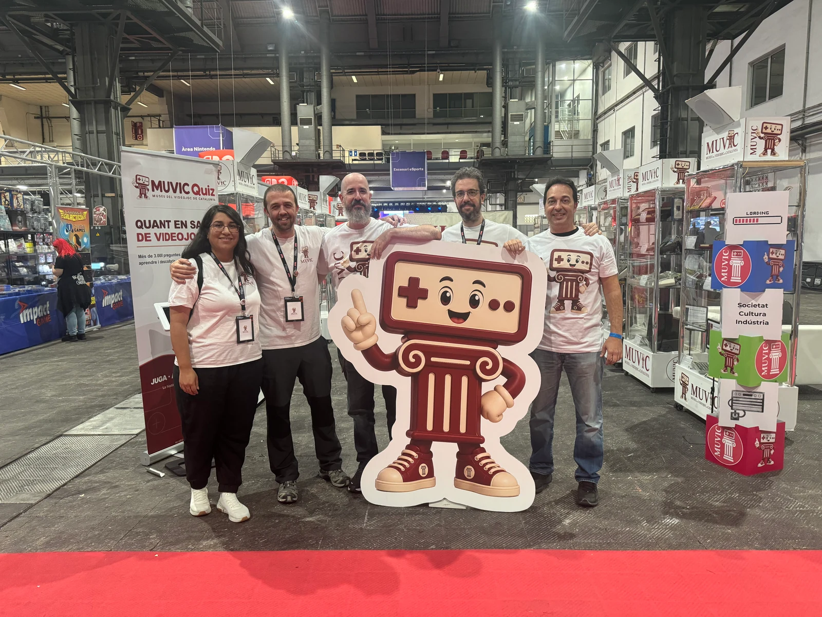 L’equip del MUVIC amb la mascota del museu davant les vitrines del SAGA Barcelona Game Fest 2026
